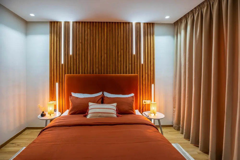 Chambre livrée, tête de lit terracotta et bardage bois éclairé, appartement à Casablanca