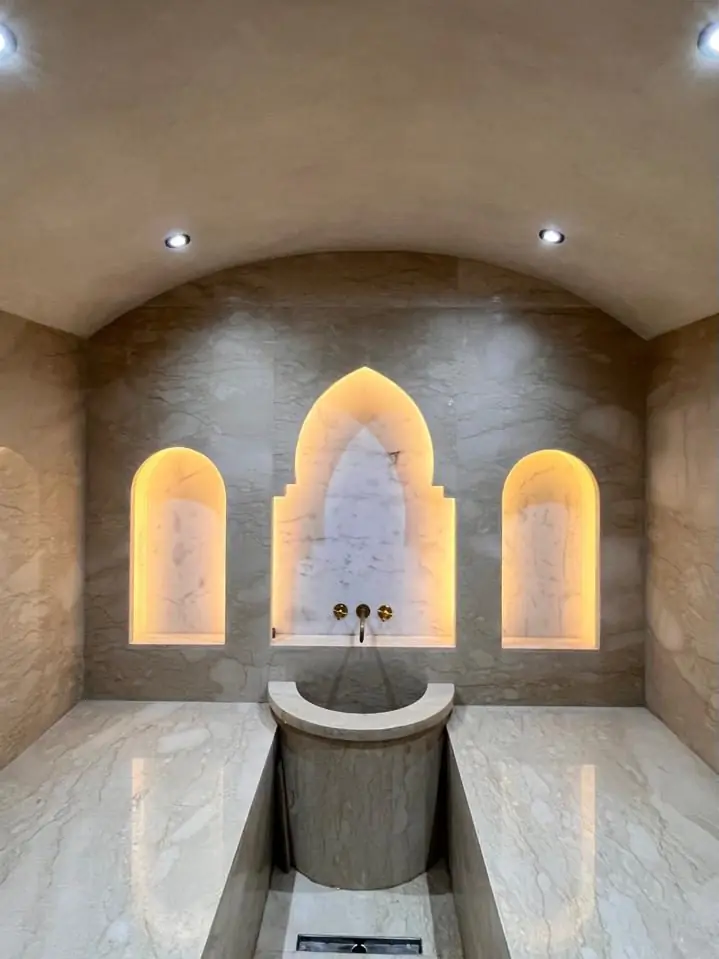 Hammam réalisé dans une villa contemporaine à Marrakech : niches en arc éclairées, vasque en pierre